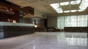 Um hall amplo com piso de mármore, balcão de recepção e área de estar com sofás.