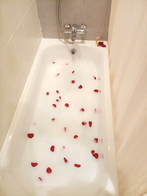 A bathtub with rose petals floating in the water.