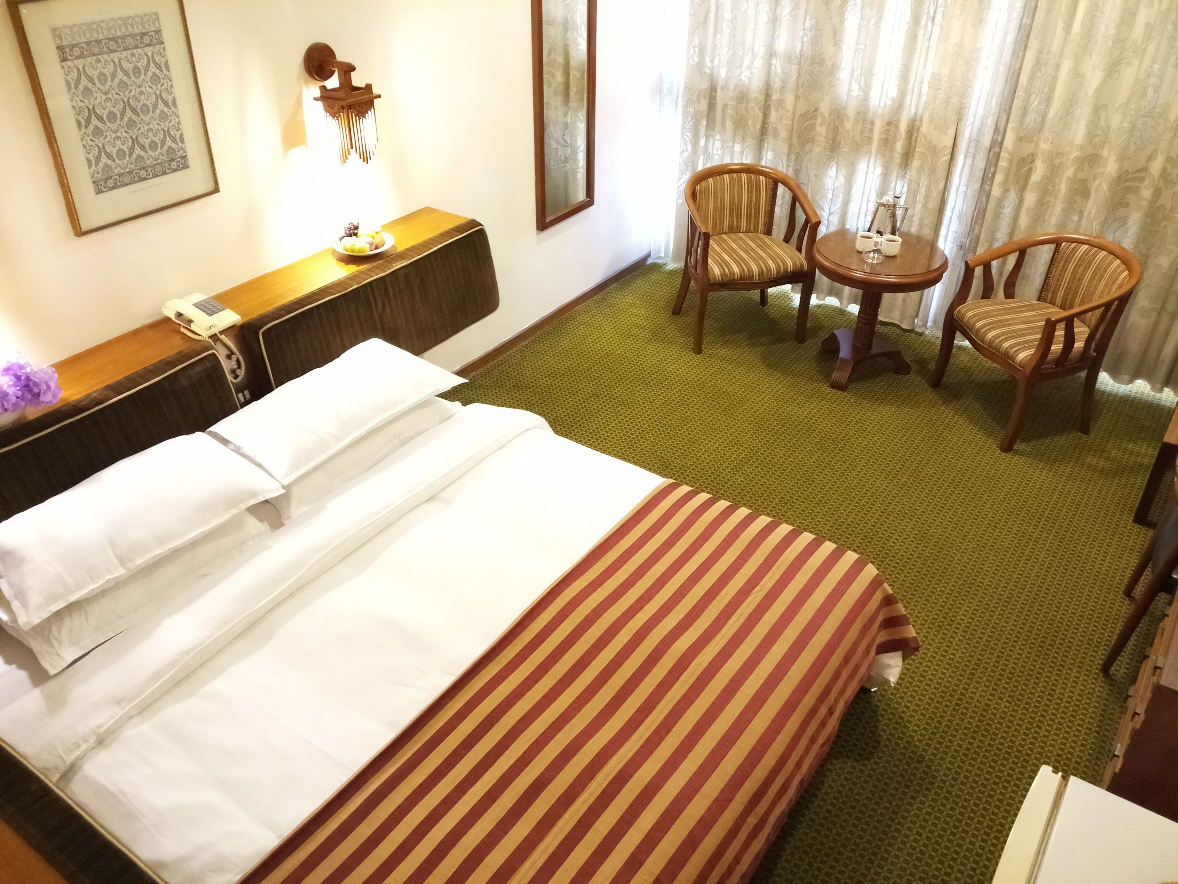 Ein Hotelzimmer mit Bett, zwei Stühlen, einem kleinen Tisch, einem Telefon und einer Wanddekoration.