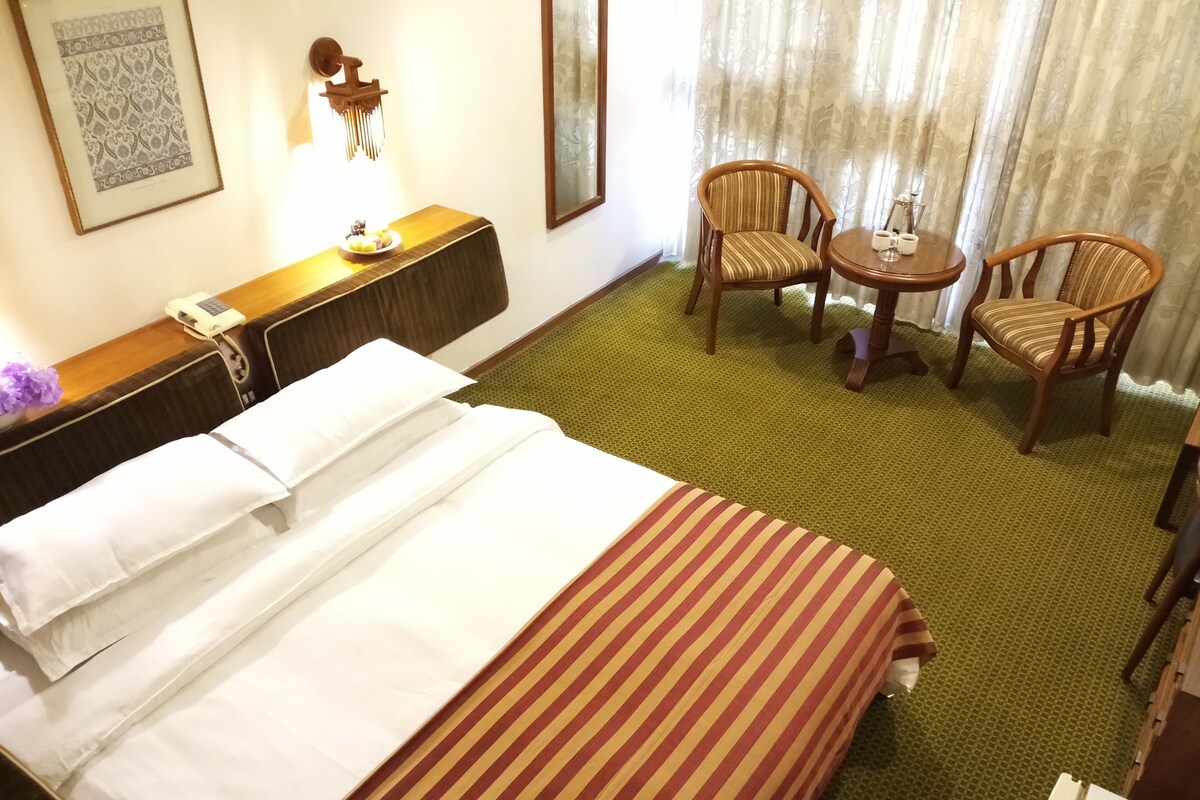 Habitación de hotel con cama, dos sillas, una mesita, teléfono y un adorno en la pared.