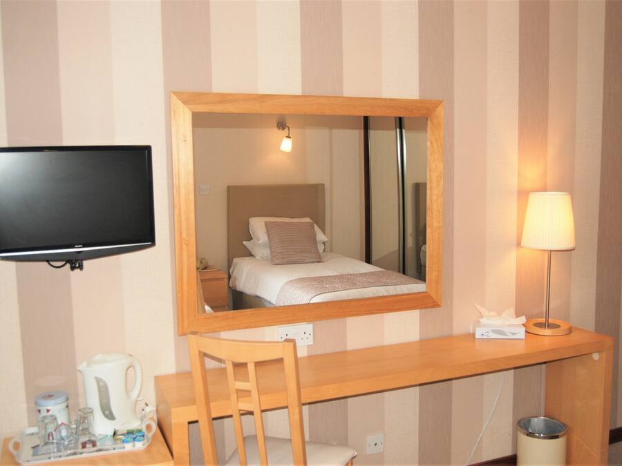 A hotel room with a bed, a television mounted on the wall, a desk with a lamp, and a trash bin.