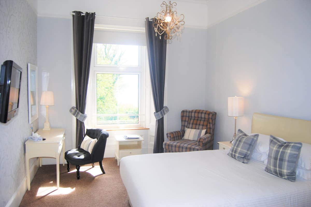 A hotel room with a bed, two chairs, a desk, a lamp, and a window with curtains.