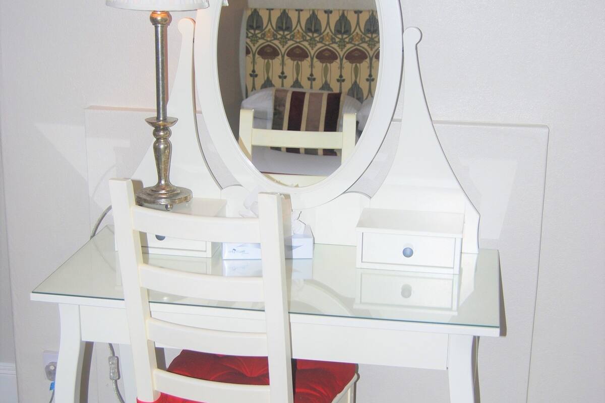 A white vanity with a mirror, a lamp, and a chair with a red cushion.