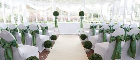 Une allée décorée pour une cérémonie de mariage, avec des chaises blanches et des rubans verts, menant à un autel blanc.