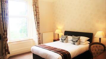 A hotel room with a large bed, two bedside lamps, a window with curtains, and a radiator.