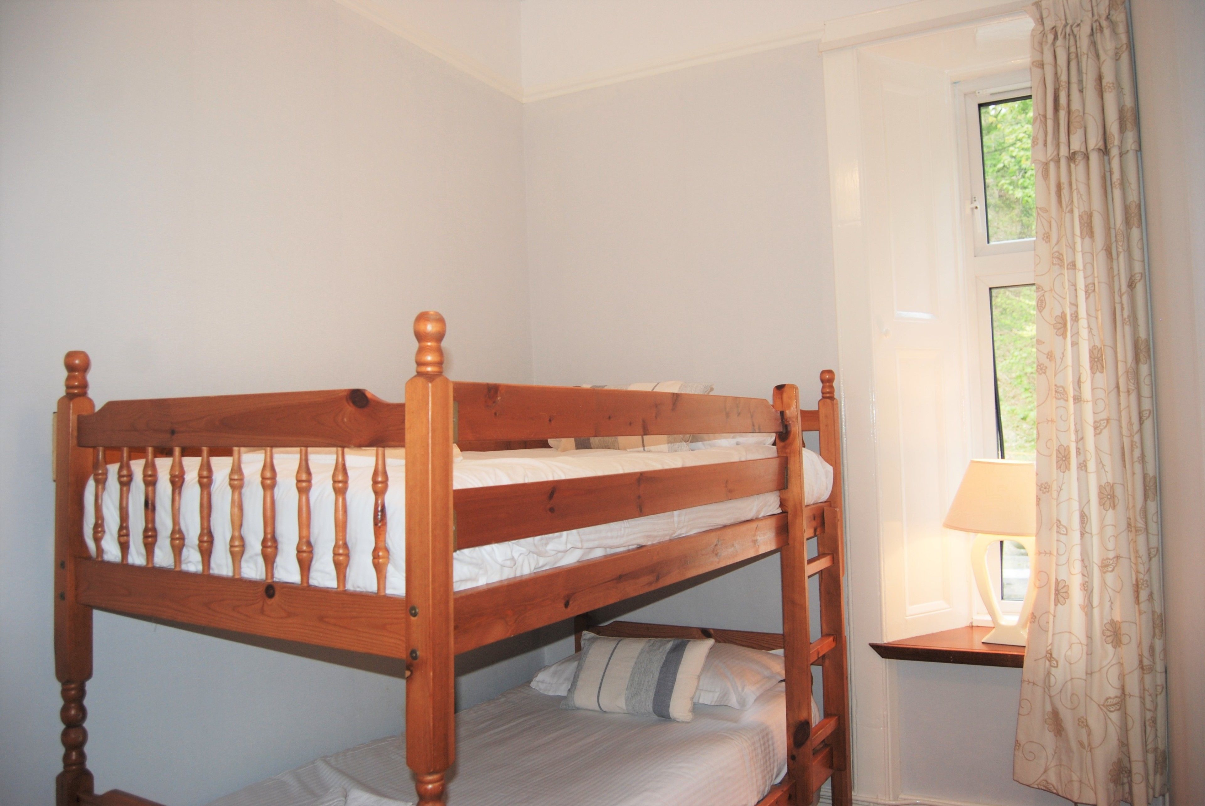 Una cama litera con estructura de madera y una mesita de noche con lámpara.
