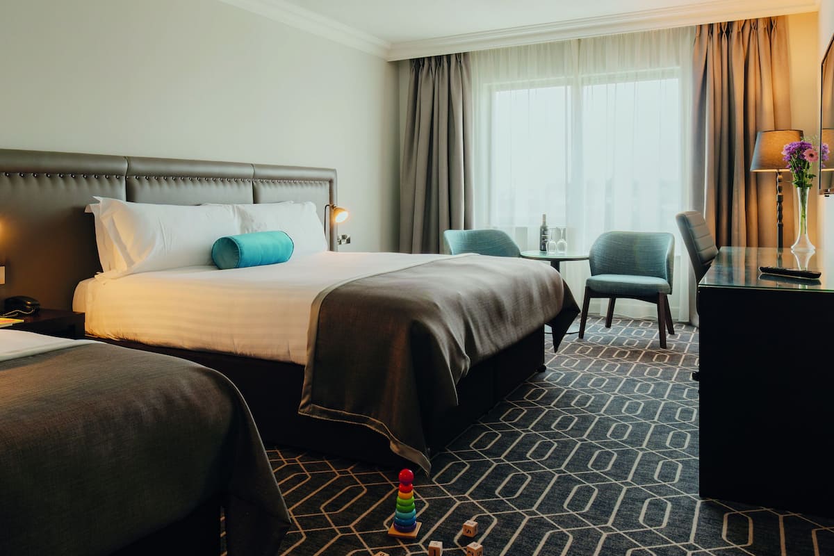 A hotel room with two beds, a desk, a chair, and a TV.