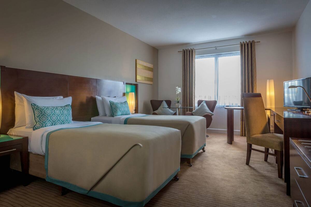 A hotel room with two beds, a desk, a chair, a television, and a window with curtains.