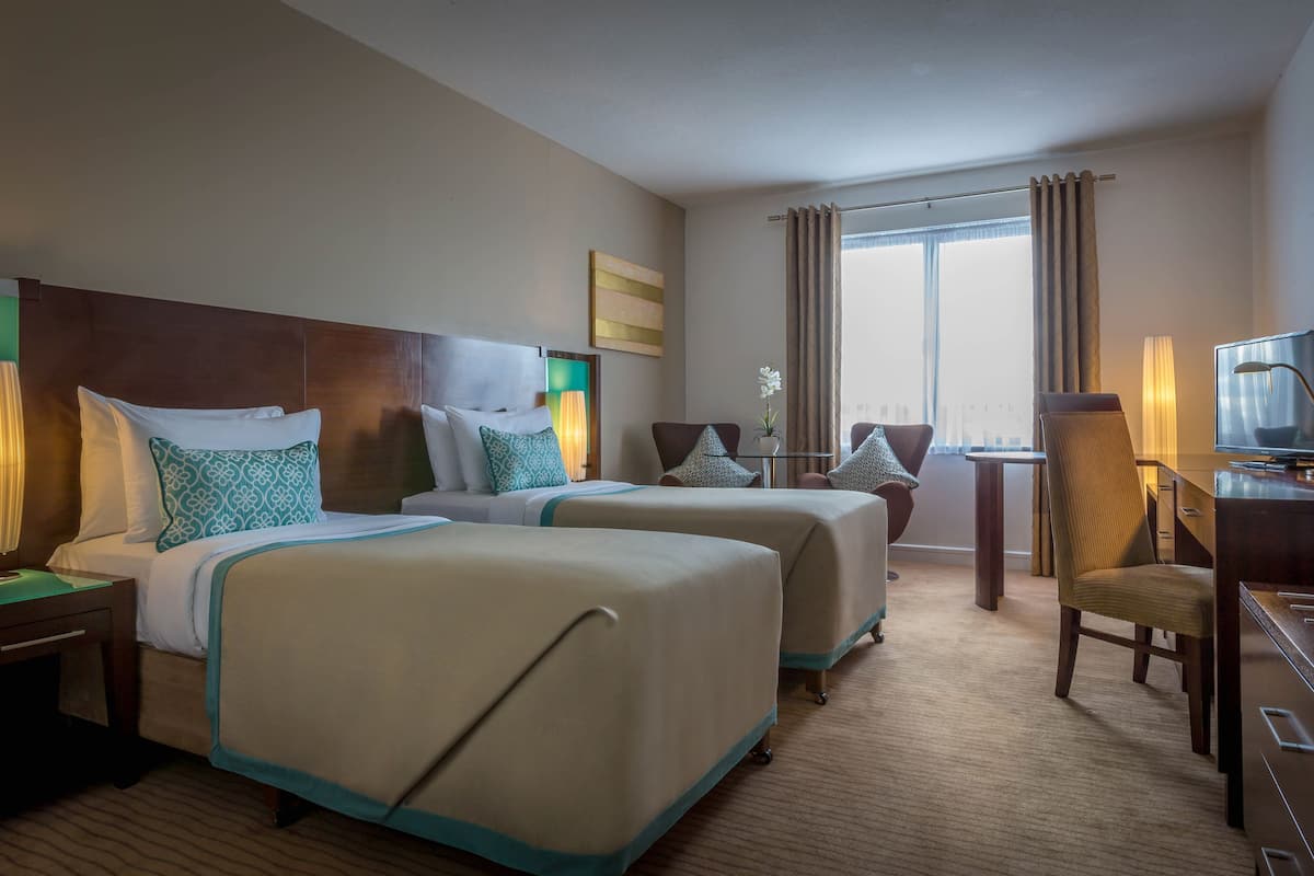 A hotel room with two beds, a desk, a chair, a television, and a window with curtains.
