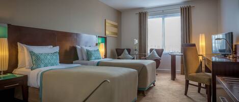 A hotel room with two beds, a desk, a chair, a television, and a window with curtains.