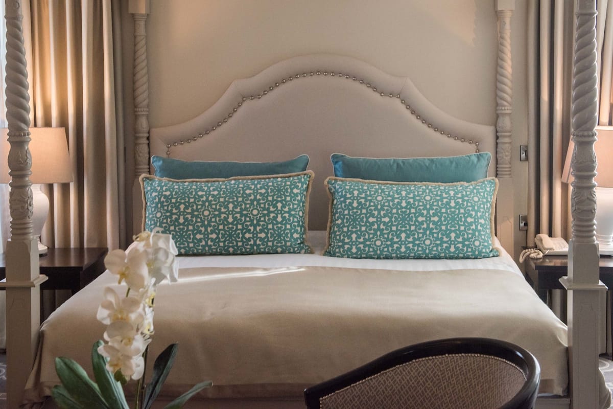 A hotel room with a large bed, two decorative pillows, a nightstand with a lamp, and a chair.