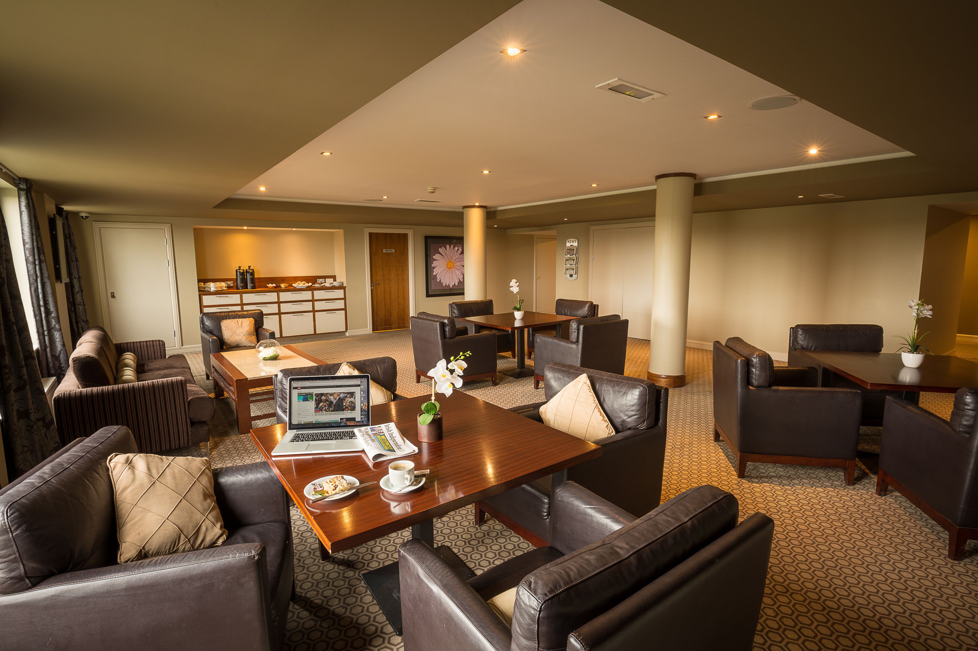 A spacious hotel lobby with leather sofas, a wooden coffee table, and a dining area.