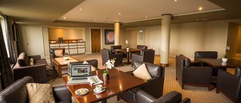A spacious hotel lobby with leather sofas, a wooden coffee table, and a dining area.