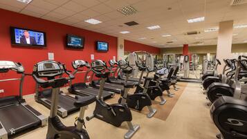 A gym with treadmills and elliptical machines, a red wall, and two televisions mounted on the wall.
