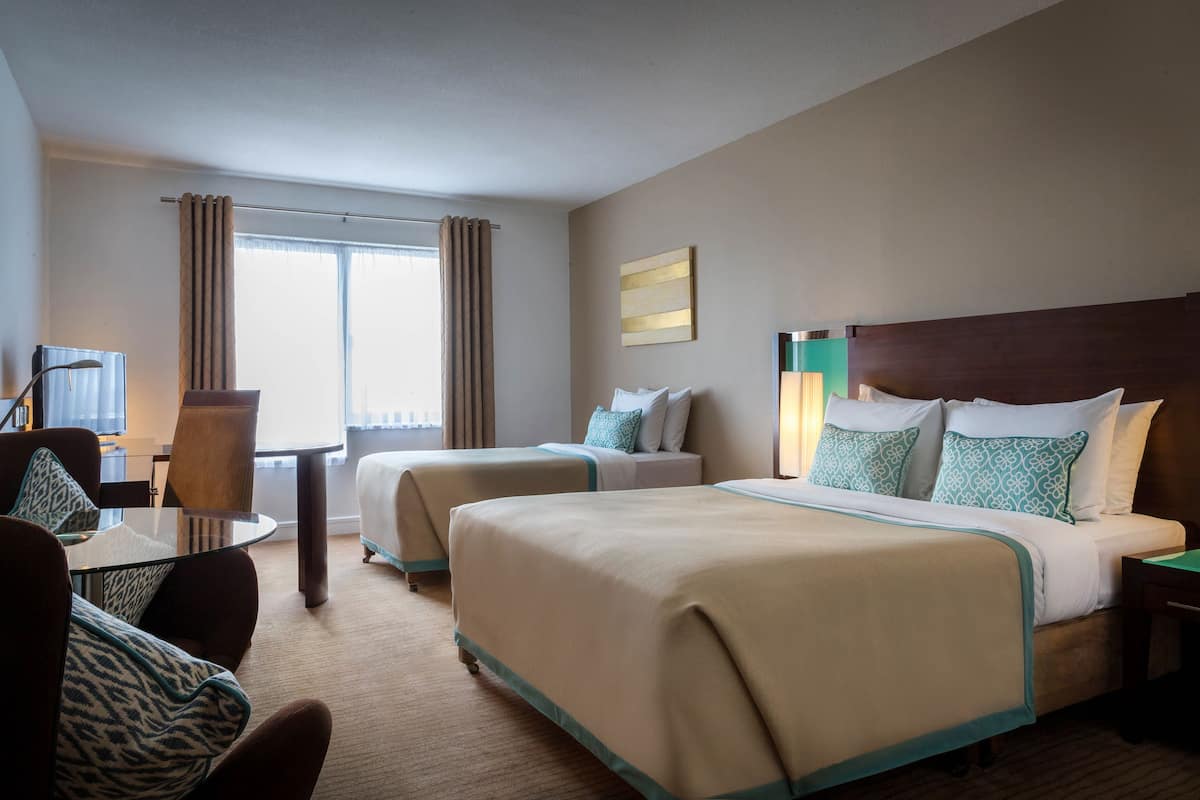 A hotel room with two beds, a desk, a chair, a television, and a window with curtains.