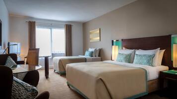 A hotel room with two beds, a desk, a chair, a television, and a window with curtains.