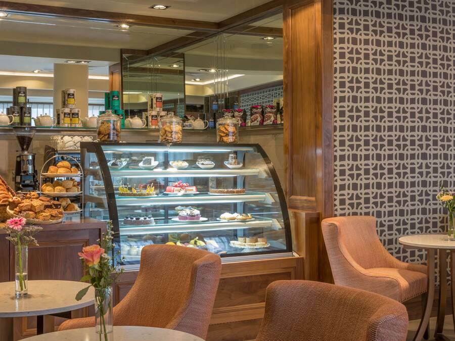 A bakery display with pastries and cakes, seating area with chairs, and a coffee machine.