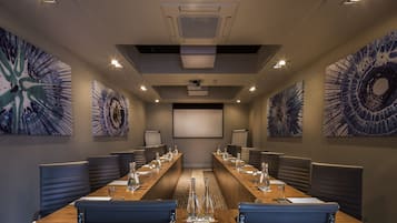 A conference room with a long table, multiple chairs, and a projector screen.