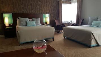A hotel room with two beds, a fishbowl on a table, and a view of the outdoors.