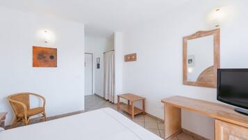 A hotel room with a bed, a wooden desk, a television, a wicker chair, and a mirror.