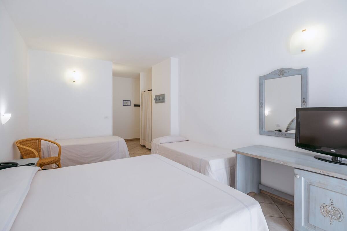 A hotel room with two beds, a desk with a TV, a chair, and a bathroom door.
