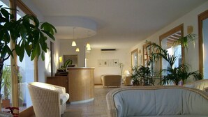 Un hall d’entrée spacieux, doté de meubles en osier, d’un comptoir d’accueil central et de plantes en pot.