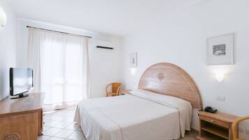 Habitación de hotel con una cama, un televisor sobre una cómoda de madera, una silla y un escritorio con teléfono.
