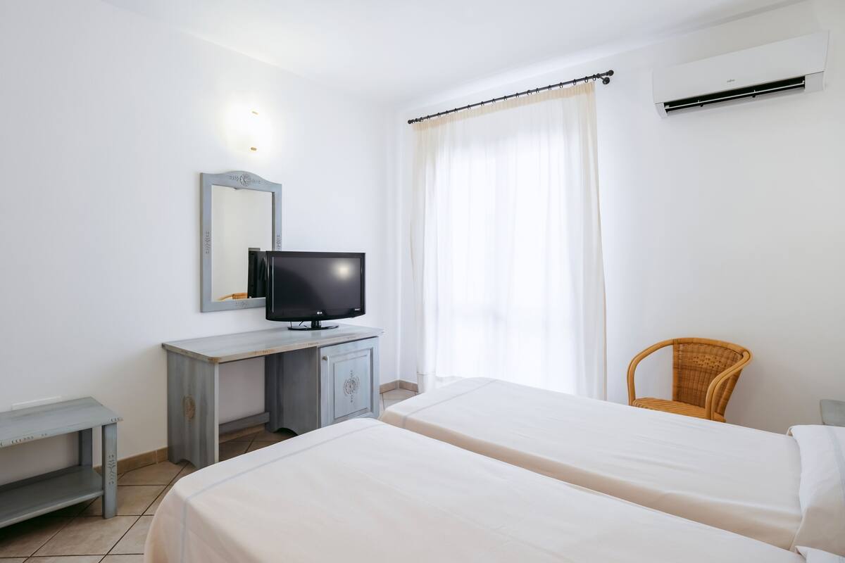 A hotel room with two beds, a desk with a television, a chair, and an air conditioning unit.