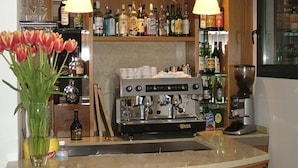 Un coin bar équipé d’une machine à café, d’étagères remplies de bouteilles d’alcool et d’un vase de tulipes.