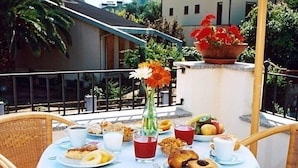 Une table dressée pour le petit-déjeuner, avec divers aliments et boissons, entourée de chaises en osier.