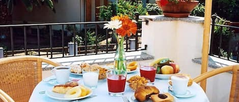 A table set for breakfast with various food items and drinks, surrounded by wicker chairs.