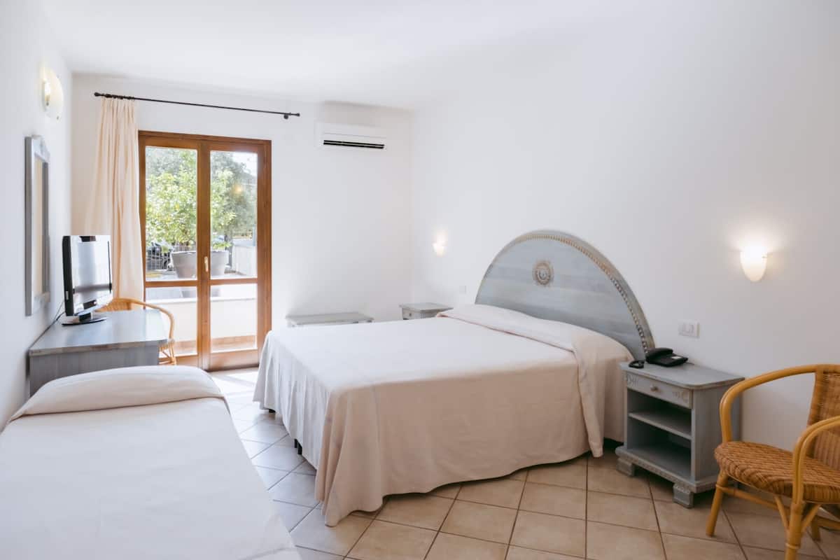 A hotel room with two beds, a desk with a computer, a chair, and a view of greenery outside.