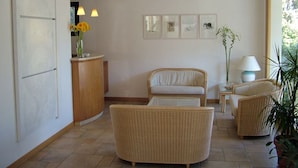 Un salon moderne avec un canapé, deux fauteuils, une petite table avec une lampe et un vase de fleurs. On y trouve également un meuble en bois orné d’un vase rempli de fleurs jaunes, ainsi qu’un mur décoré de tableaux encadrés.