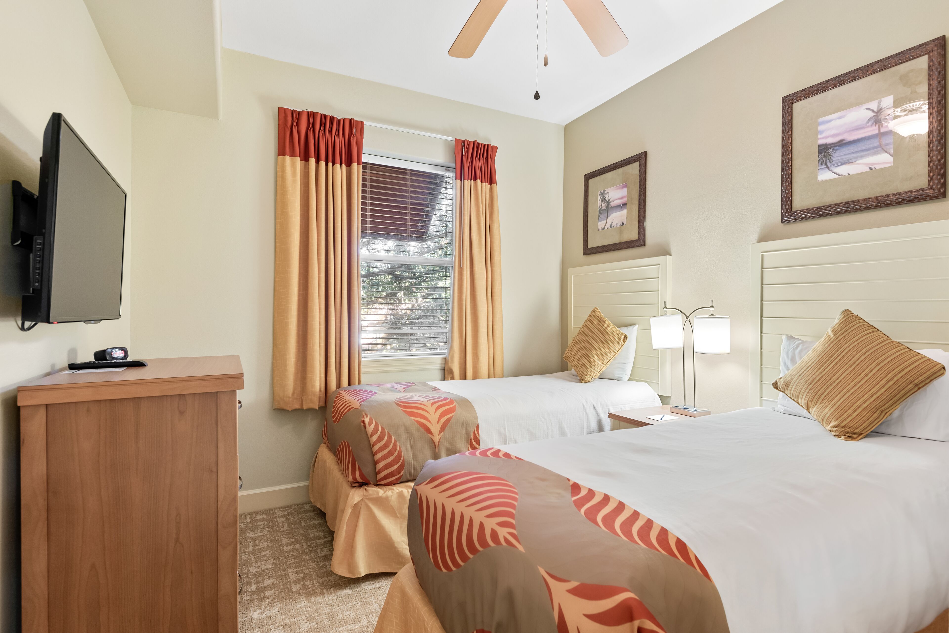 A hotel room with two beds, a desk, a TV, and a window with curtains.