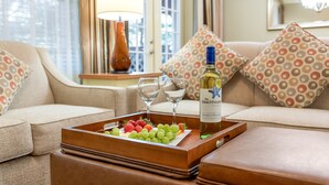 Een dienblad met druiven en aardbeien op een houten tafel, een fles wijn en twee wijnglazen op een beige bank.