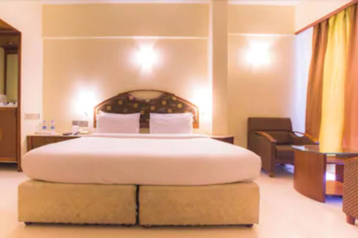 Una cama grande con cabecera, una mesita de noche y una silla en una habitación de hotel.