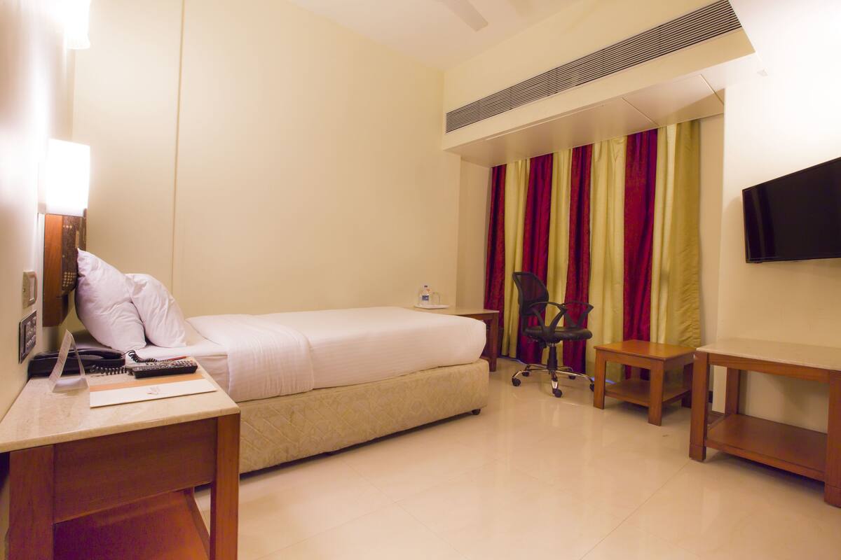 Una habitación de hotel con cama, escritorio, silla, televisor y cortinas.
