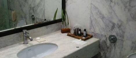 Un baño con lavamanos de mármol, un espejo y un inodoro.