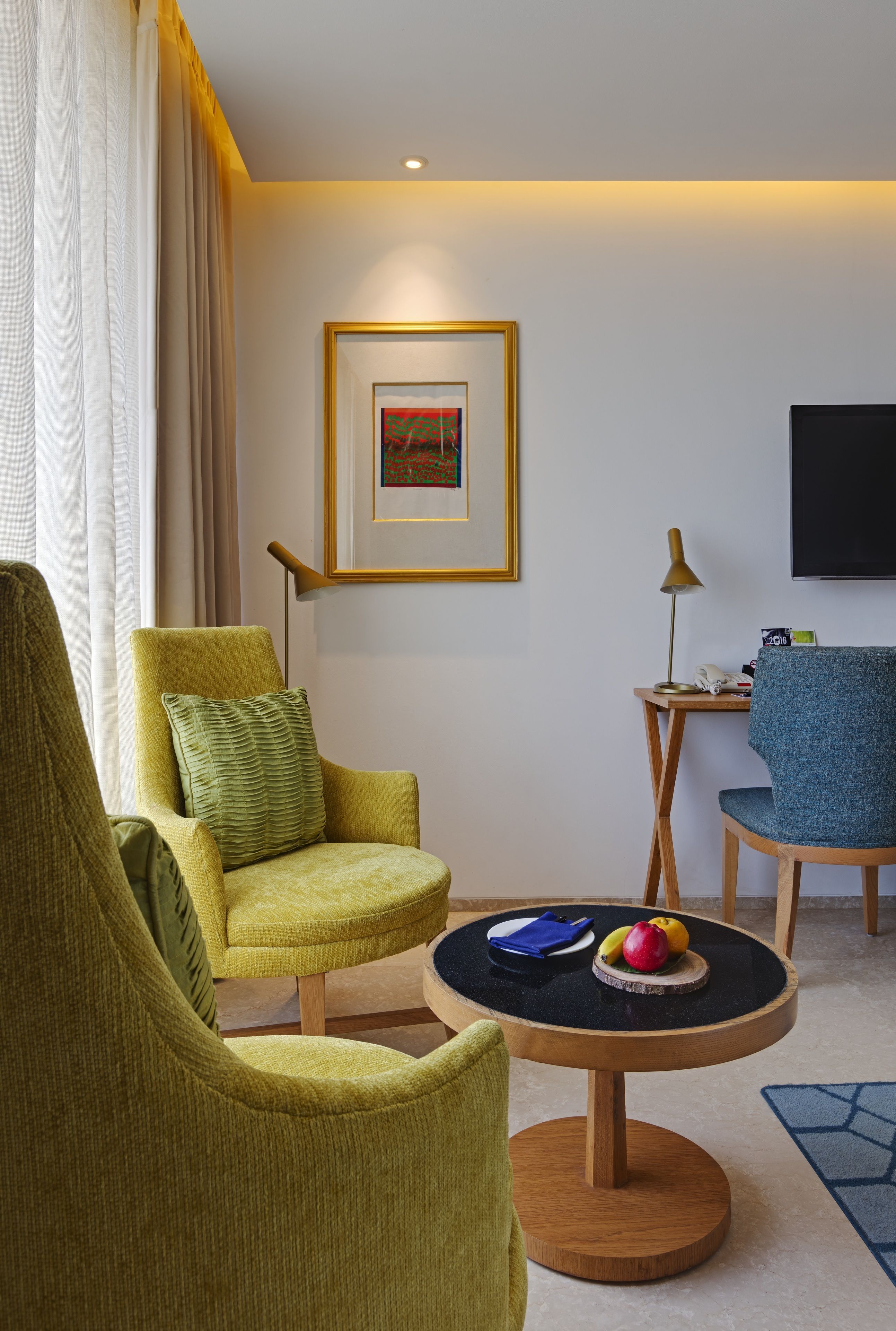 Un salon moderne avec deux fauteuils, une table basse ronde sur laquelle sont disposés des fruits, un tableau encadré au mur et un téléviseur à écran plat.