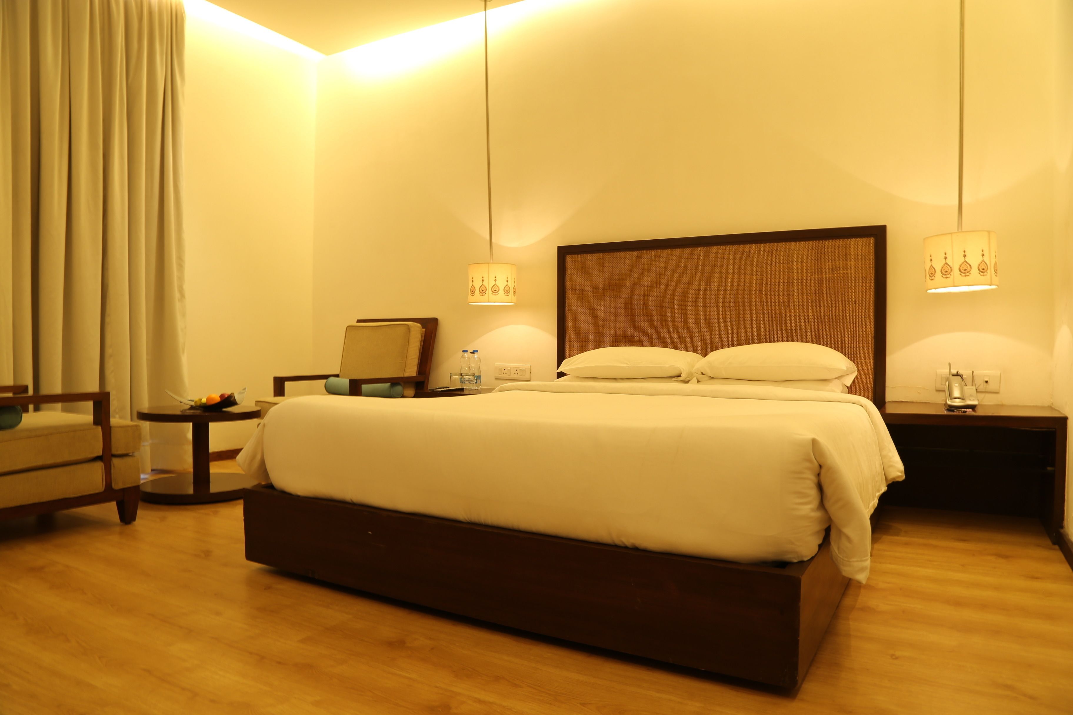 Una habitación de hotel con una cama grande, dos mesitas de noche, una silla y una pequeña mesa con lámpara.