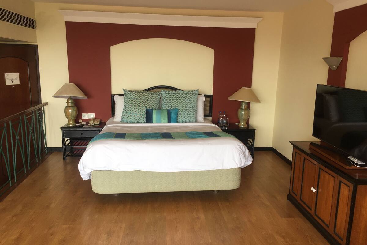 Una habitación de hotel con una cama grande, dos mesitas de noche, un televisor y una pared decorada en rojo.