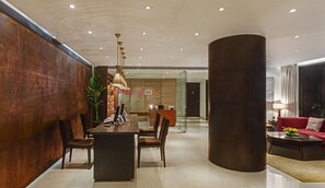 Ein moderner Empfangsbereich mit einem Holzbüro, einer großen Pflanze in einem Topf sowie einer Sitzecke mit einem roten Sofa und einem Couchtisch.