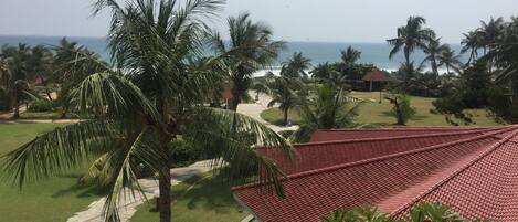 A resort with a red-roofed building, palm trees, and a view of the ocean.