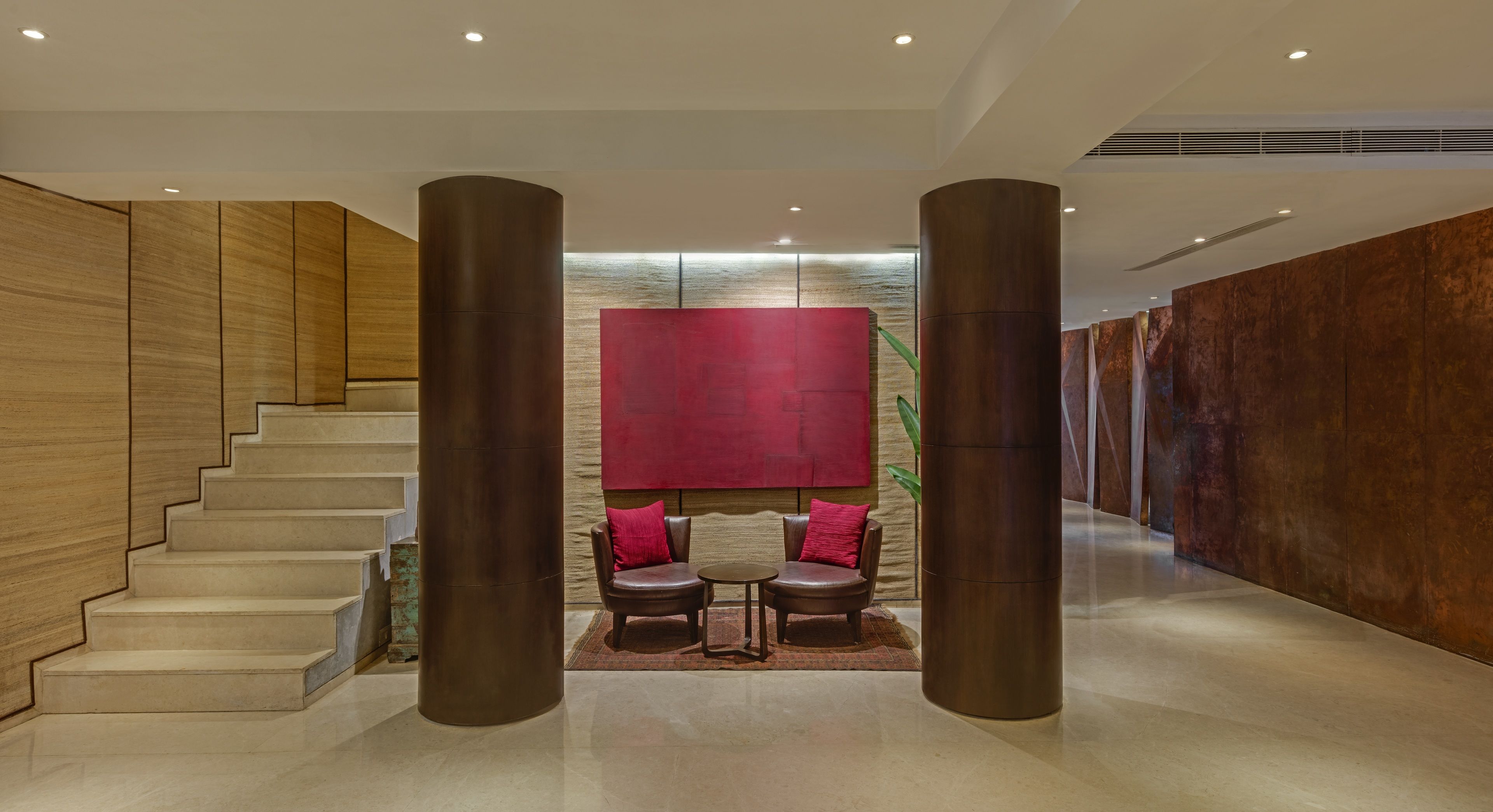 A modern lobby with a staircase, a red artwork, two leather chairs, and a large column.