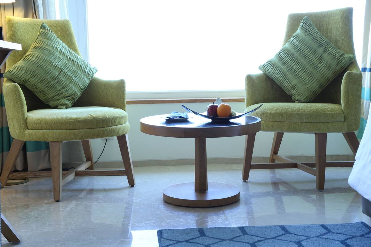 Una habitación con dos sillones verdes, una mesita redonda con un frutero y una alfombra estampada.