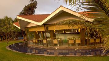 Un restaurante con terraza, piscina y jardín tropical.