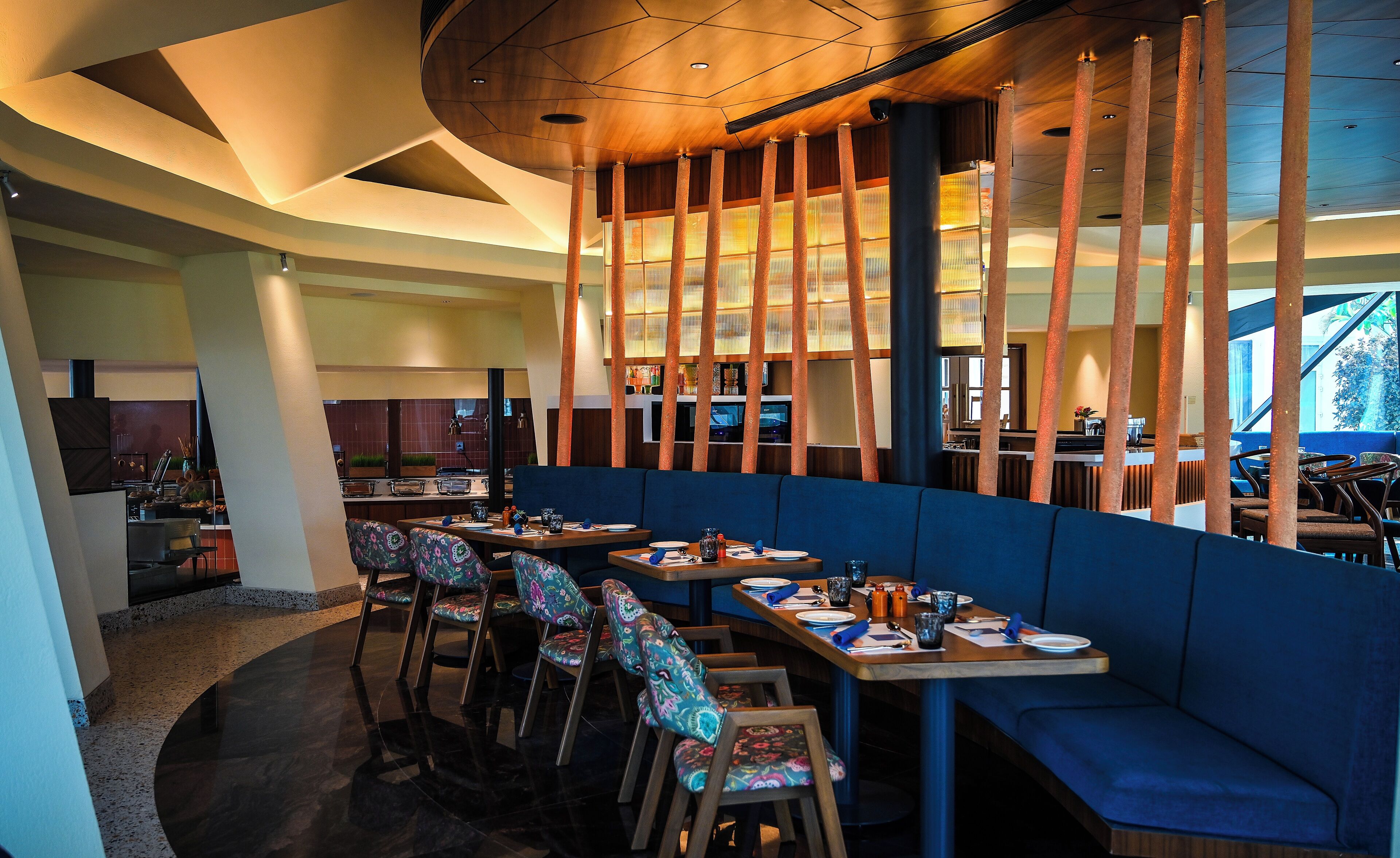 Een restaurant met een modern interieur, met een lange toonbank, meerdere zithoeken en een zichtbare keuken op de achtergrond.