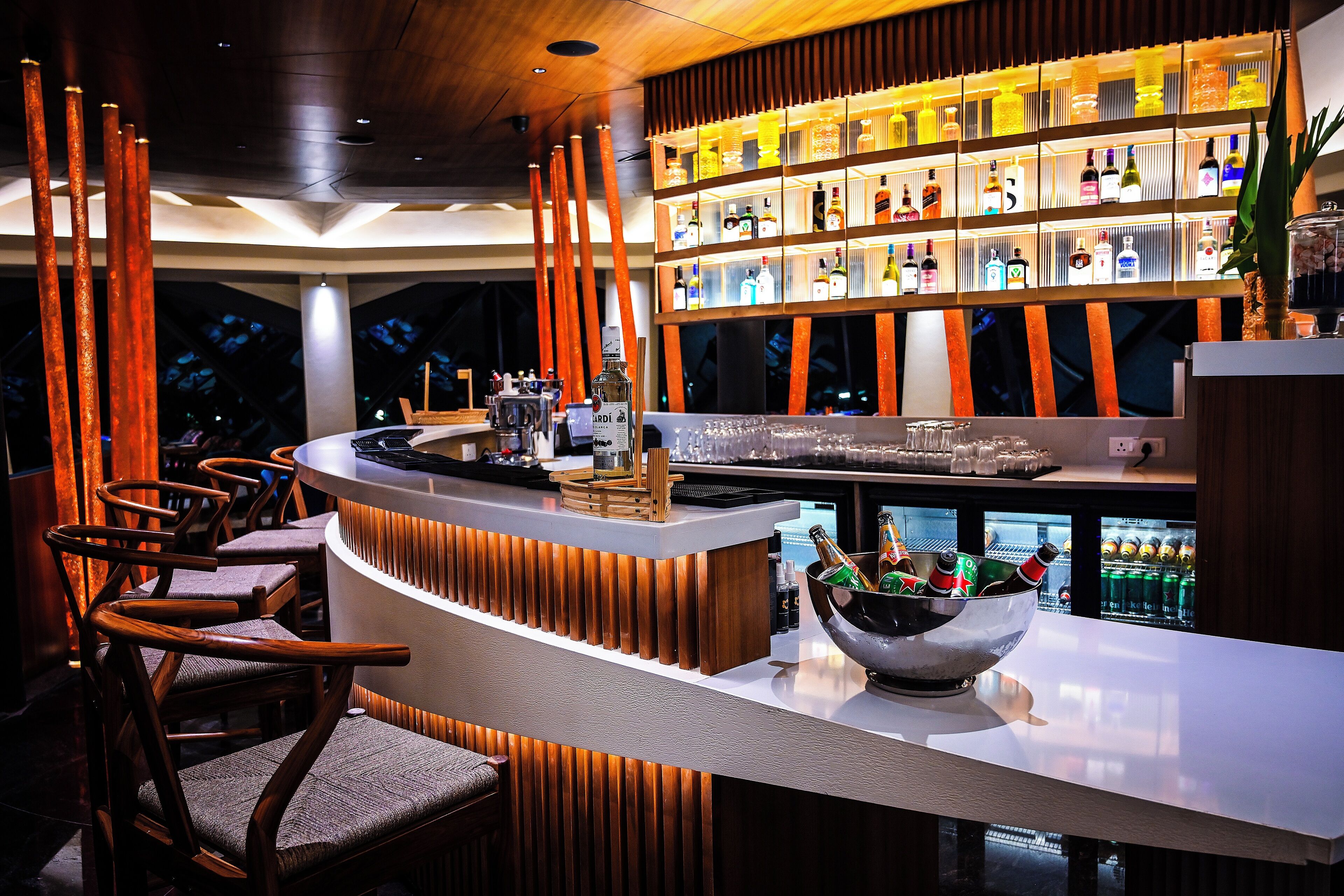 A bar area with wooden chairs, a counter with a bowl of bottles, and shelves of liquor bottles.