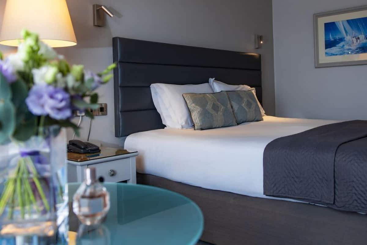 A hotel room with a bed, bedside lamp, nightstand, and a round table with a vase of flowers.