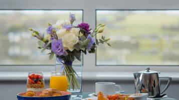 A breakfast table with a vase of flowers, a glass of orange juice, a cup, a bowl of croissants, and a plate of food.
